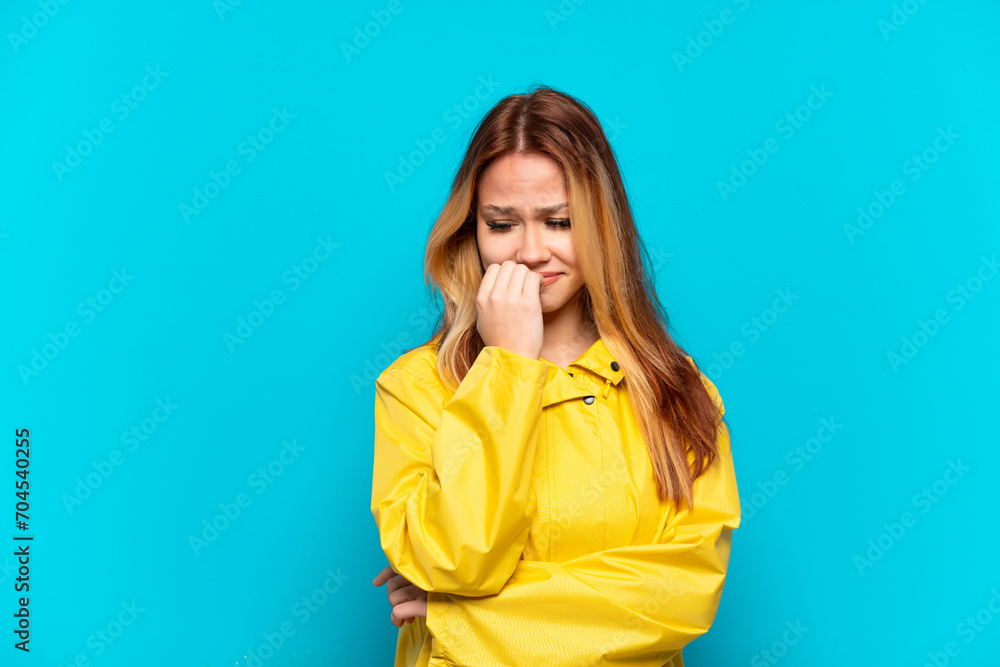 Teenager girl wearing a rainproof coat over isolated blue background having doubts Teenager girl wearing a rainproof coat over isolated blue background having doubts