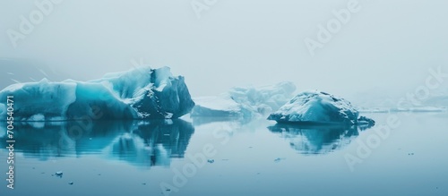 Frozen blue icebergs drift in calm ocean waters, creating a picturesque icy winter landscape during foggy weather in Iceland.