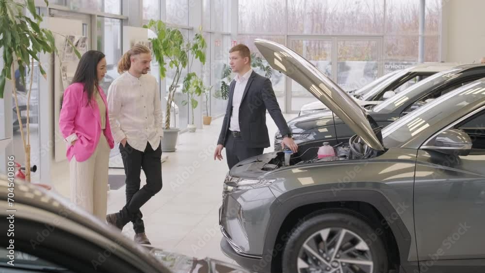 Young car salesman showing to young couple new automobile at dealership salon. Young car salesman showing to young couple new automobile at dealership salon.