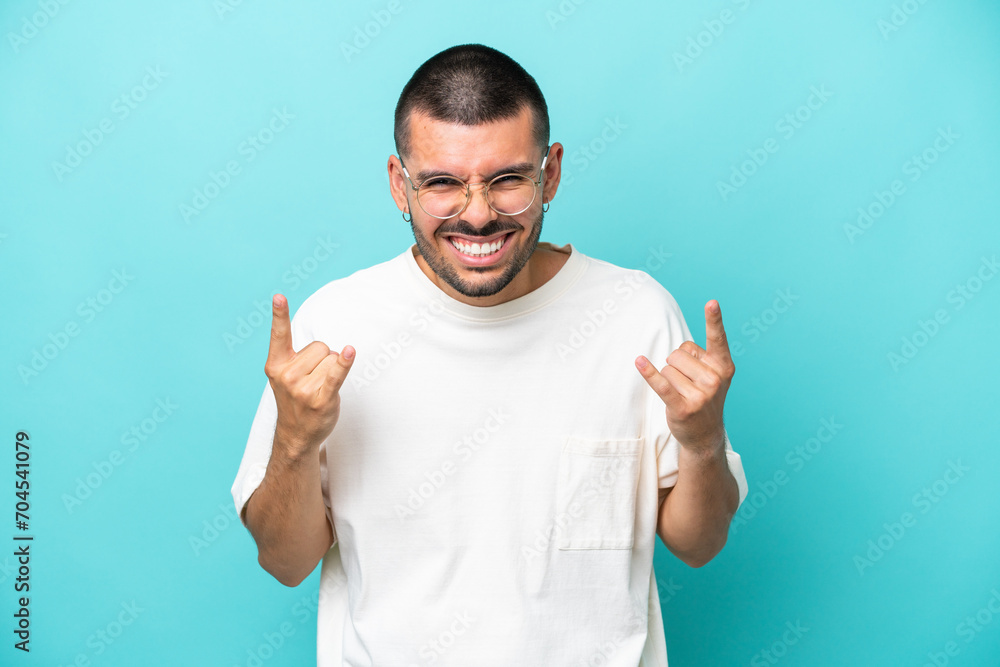 Young caucasian man isolated on blue background making horn gesture Young caucasian man isolated on blue background making horn gesture