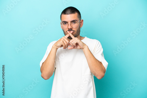 Young caucasian man isolated on blue background showing a sign of silence gesture