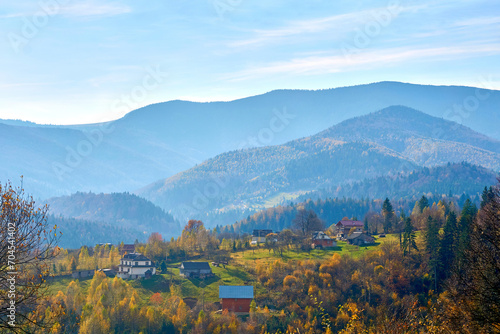 Aerial view of an autumn small village in a valley and mountains in a blue haze