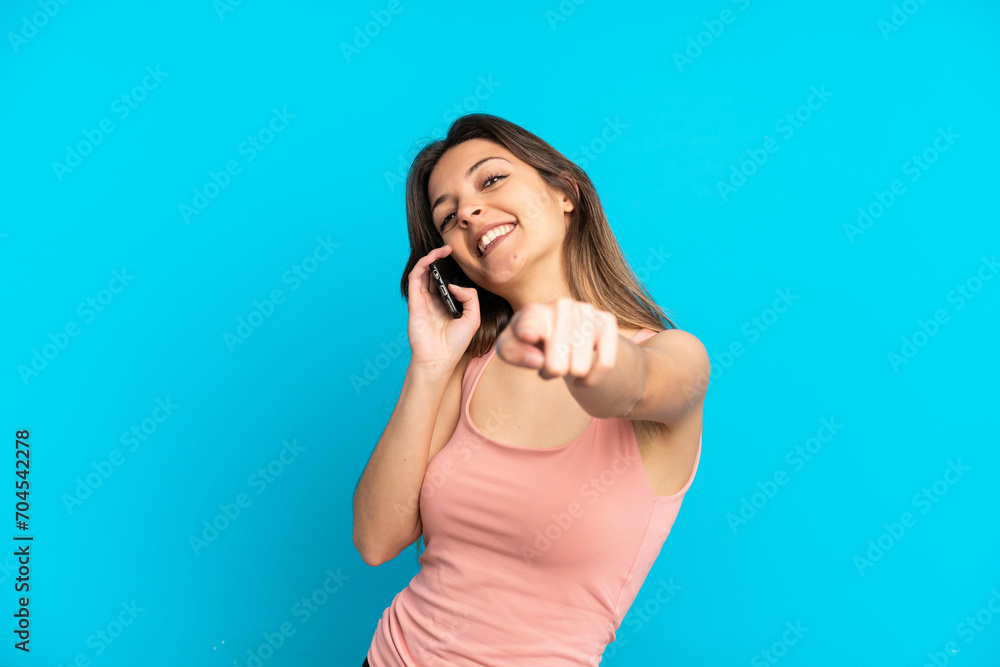 Fototapeta premium Young caucasian woman using mobile phone isolated on blue background pointing front with happy expression