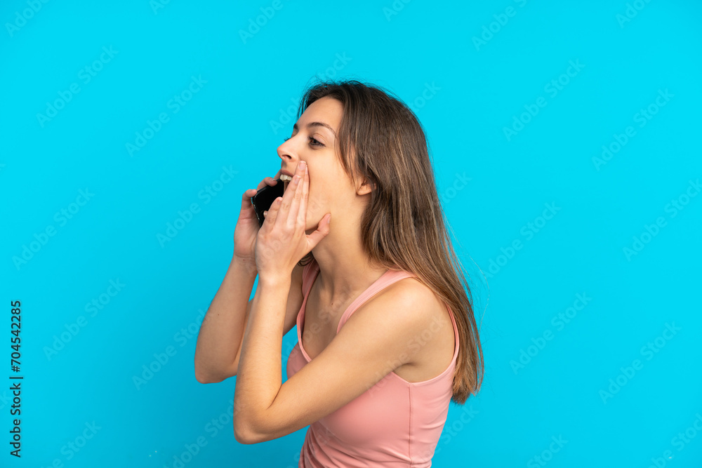 Young caucasian woman using mobile phone isolated on blue background shouting with mouth wide open to the side Young caucasian woman using mobile phone isolated on blue background shouting with mouth wide open to the side