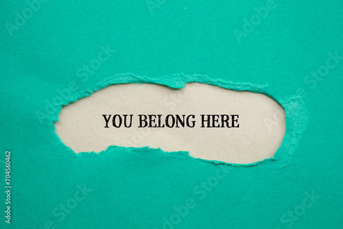 You belong here lettering on ripped blue paper with gray background. Conceptual business photo. Top view, copy space for text.
