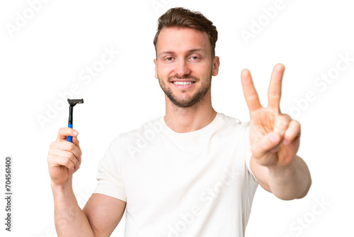 Young caucasian man shaving his beard over isolated chroma key background smiling and showing victory sign