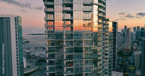 Glass skyscraper in center Miami at sunset against background of Atlantic ocean and promenade with ferris wheel. Reflections in windows of sky. Aerial view of evening city with houses. photo