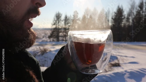 A man with a beard drinking tea in the cold. There is a strong steam coming from the cup of tea.  