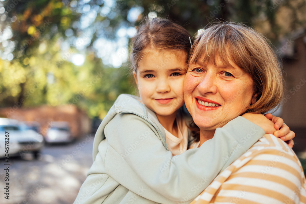 Little girl hugging smiling middle aged woman. Cute female kid and her grandmother enjoy walking outdoors Little girl hugging smiling middle aged woman. Cute female kid and her grandmother enjoy walking outdoors