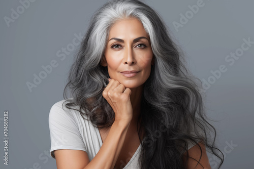 Gorgeous senior older Indian woman with long silver hair and natural makeup touching her face