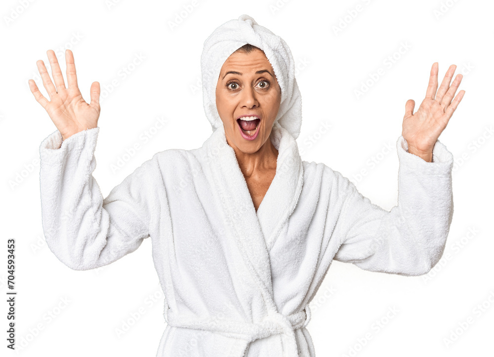 Middle-aged woman with towel post-shower in studio receiving a pleasant surprise, excited and raising hands. Middle-aged woman with towel post-shower in studio receiving a pleasant surprise, excited and raising hands.
