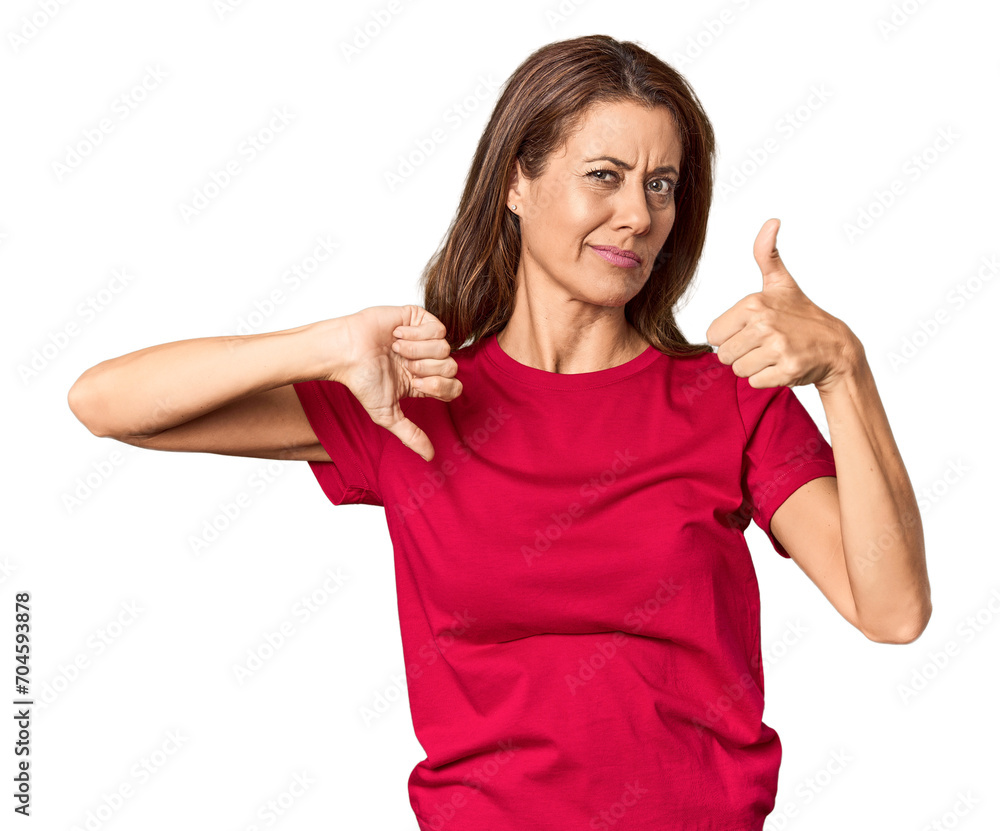 Middle-aged woman portrait in studio setting showing thumbs up and thumbs down, difficult choose concept Middle-aged woman portrait in studio setting showing thumbs up and thumbs down, difficult choose concept
