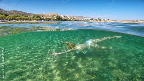 Young woman swims at the bottom of the beach Livadakia on half underwater view in Serifos, Greece