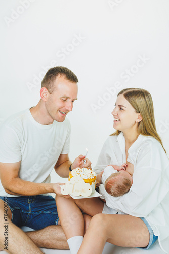 Young happy parents with a baby in their arms and a cake celebrate the first month of the baby s life. Mom and dad with a newborn baby on a white background