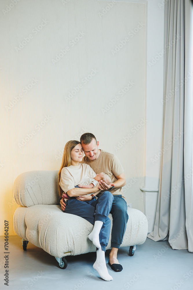 Young happy parents with a newborn baby in their arms at home on the couch. Mom and dad with a newborn baby on a white background
