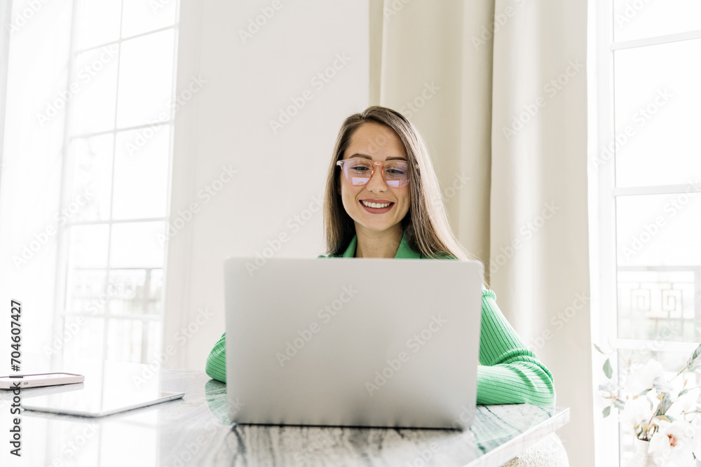 Radiant woman working on laptop in a light-filled room, with a tablet and smartphone on the marble table. Radiant woman working on laptop in a light-filled room, with a tablet and smartphone on the marble table.