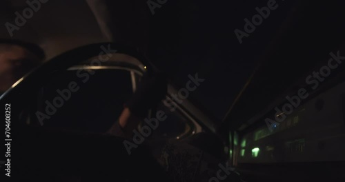 Horror night scene of a young serious punk guy drives a damaged car off-road, view beside an old steering wheel. Vehicle shakes in time of move because of corrugation on the way photo