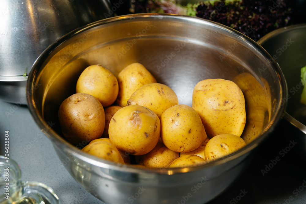 Raw Potatoes in a Metal Bowl for Cooking. A bowl full of unpeeled raw yellow potatoes, a staple ingredient for many recipes, on a kitchen countertop. Raw Potatoes in a Metal Bowl for Cooking. A bowl full of unpeeled raw yellow potatoes, a staple ingredient for many recipes, on a kitchen countertop.