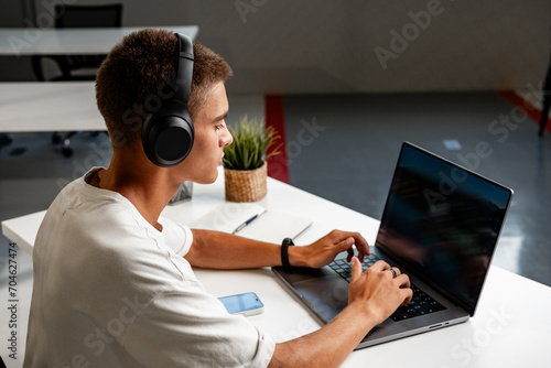 Young man wearing headphones while studying with laptop photo