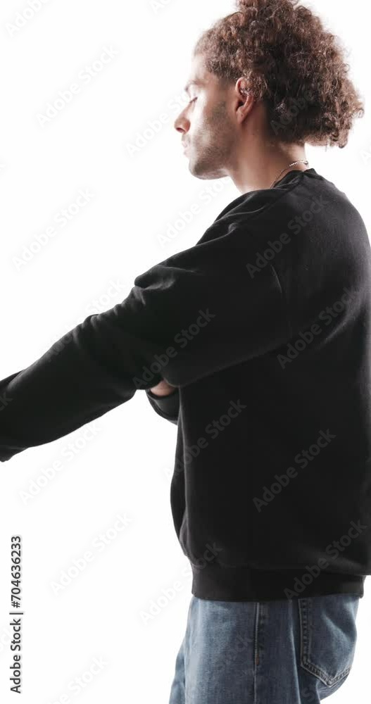 sexy casual man with curly hair adjusting sweatshirt sleeves and collar while being cool and posing in a confident way on grey background sexy casual man with curly hair adjusting sweatshirt sleeves and collar while being cool and posing in a confident way on grey background