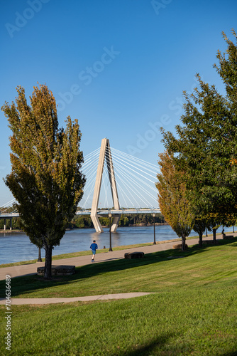 Adult man running on riverfront greenway with bridge in background 