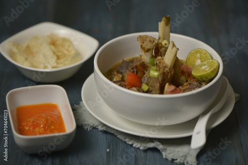 A bowl of lamb feet soup, served with brown rice and emping crackers as side dishes.