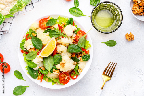 Fresh vegan cauliflower salad with baked red paprika, cherry tomatoes, spinach with walnuts on white table background, top view