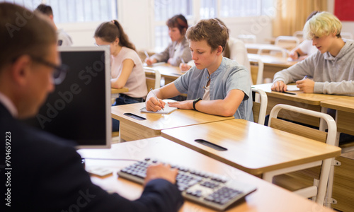 Diligent teenage high school student studying in college with classmates, making notes of teacher lecture..