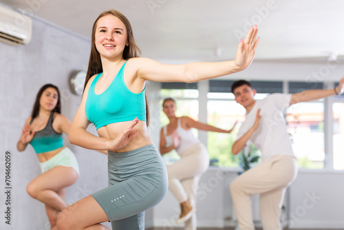 Cheerful slim teenage girl practicing energetic dance movements with group of teens in choreography class ..