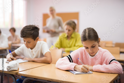 Young pupils, boy and girl, sitting at desk together and doing exercises during lesson.