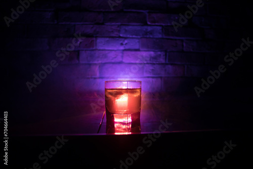 Whiskey in fire concept. Glass of whiskey and ice on wooden surface with color light and fog on background. Close up. Selective focus photo