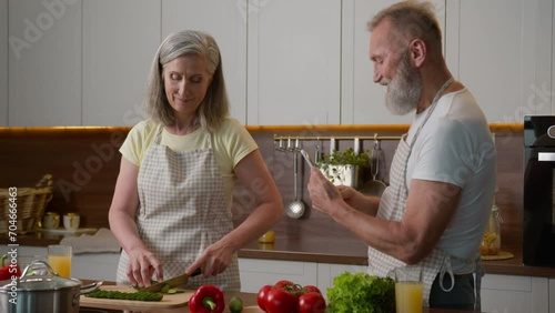 Caucasian couple middle-aged family woman man cook breakfast in home kitchen senior wife chop fresh vegetables healthy food mature husband take photo record video blog on mobile phone cooking dinner photo