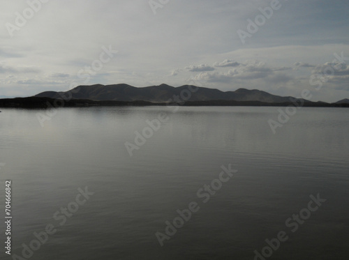 Cloudy day on a calm lake with mountains in the background © Marcos Lucio