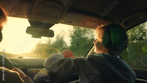 Two happy women in car listening to radio, driving towards sun. Youth, friendship, vacation travel at sunset, Concept. Female students driving in car listening to musical song on way sing and dance.
