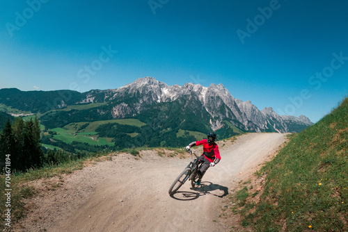 Downhill mountain biking in front of mountain scenery of Wilder Kaiser in the mountains of Austria, sunny blue sky day.