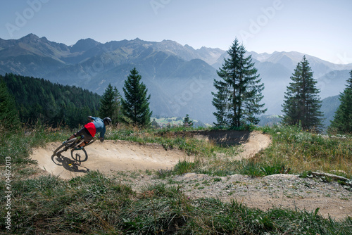 Downhill mountain biking on a shaped bike park trail in Austria, sunny blue sky day, trees and mountains in background.