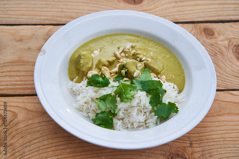 Sweet indian korma curry made from lamb meat, coconut milk, casheew nuts and lot of vegetables served with basmati rice and green coriander leaves in the deep rustic porceain plate on the wooden table