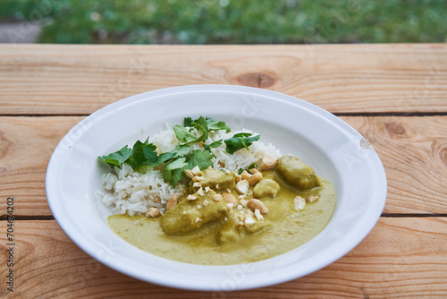 Sweet and spicy lamb curry, traditional recipe from Indian cuisine made from lamb meat, coconut milk, vegetables and cashew nuts with basmati rice and served outdoor in garden on rustic wooden table.