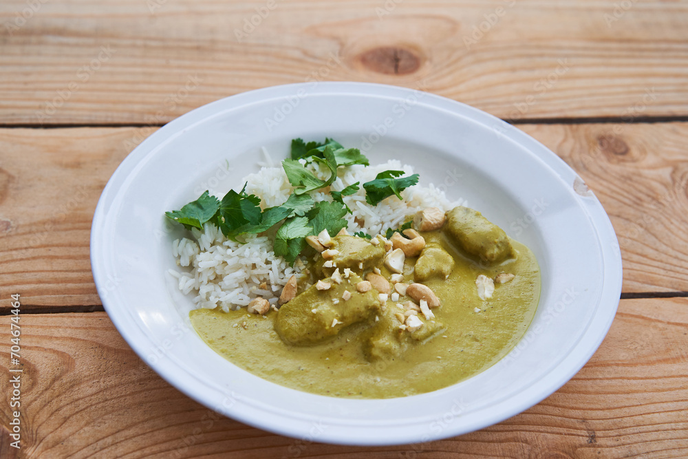 Delicius sweet and spicy green mutton curry from indian cuisine made from lamb meat, cashew nuts, yellow chilli peppers and coconut milk and served in vintage deep porcelain plate with basmati rice. 