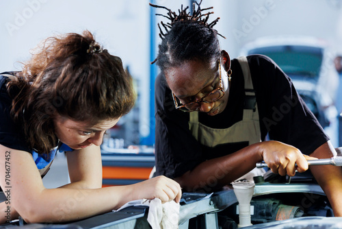 BIPOC mechanics collaborating on servicing broken vehicle, checking for faulty radiator. Women in auto repair shop working together on fixing car, discussing best options