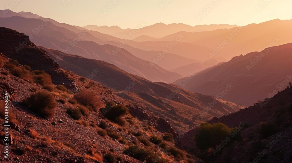  the sun is setting over the mountains in a valley with sparse grass and bushes on the side of the mountain.