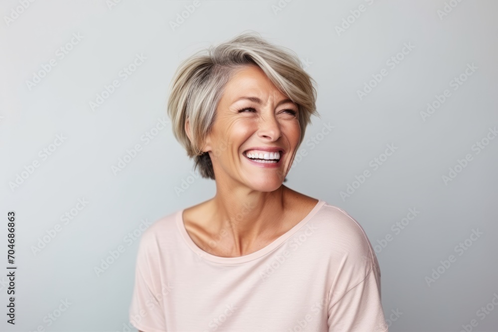Portrait of a happy mature woman laughing against a grey background. Portrait of a happy mature woman laughing against a grey background.