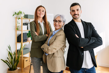 Portrait of successful small group of business people smiling at camera at office. Empowered mature businesswoman standing with young adult coworkers as a team at workplace.
