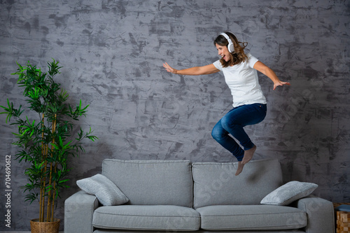 Woman jumping on the sofa while listening to music with headphones