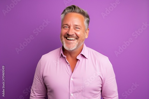 Portrait of a happy senior man laughing and looking at camera on purple background