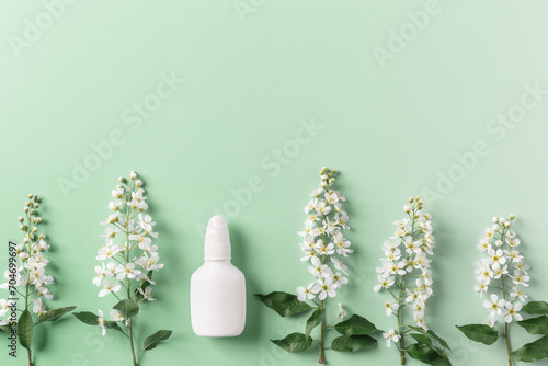 Seasonal spring allergies, fresh spring blooming branches tree and mock up white nasal spray bottle on green background, top view, minimal flat lay style. Seasonal allergy treatment concept. photo