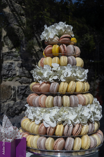 A pyramid or tier tower of an assortment of pastel colored French macaroons for a wedding. The pattern of traditional cream filled macarons is divided by a layer of white flowers on a vintage tray.  