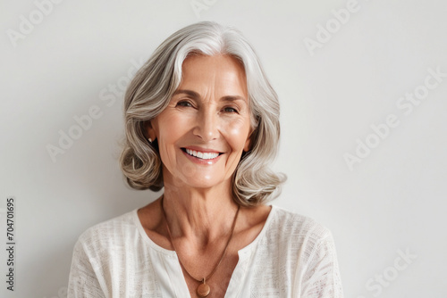 Portrait of beautiful older woman smiling and standing by white wall. A place for text, a banner for advertising. photo