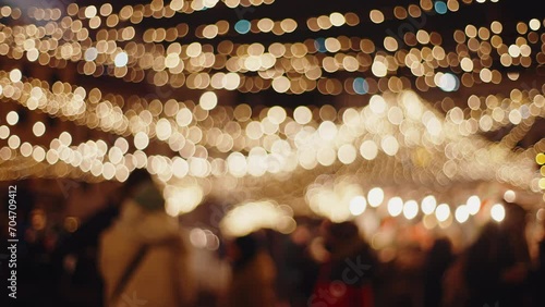 Defocused blurred Christmas background view of winter city street decorated with festive lights New Year's illumination decorations and unrecognizable people crowd walking through xmas market