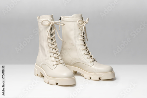 Pair of stylish white boots for women on light gray background. Trendy military beige boots on high platform with laces. Female fashion and shoes still life